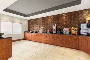 A modern kitchen with wooden cabinets, a coffee station, and a fruit display.