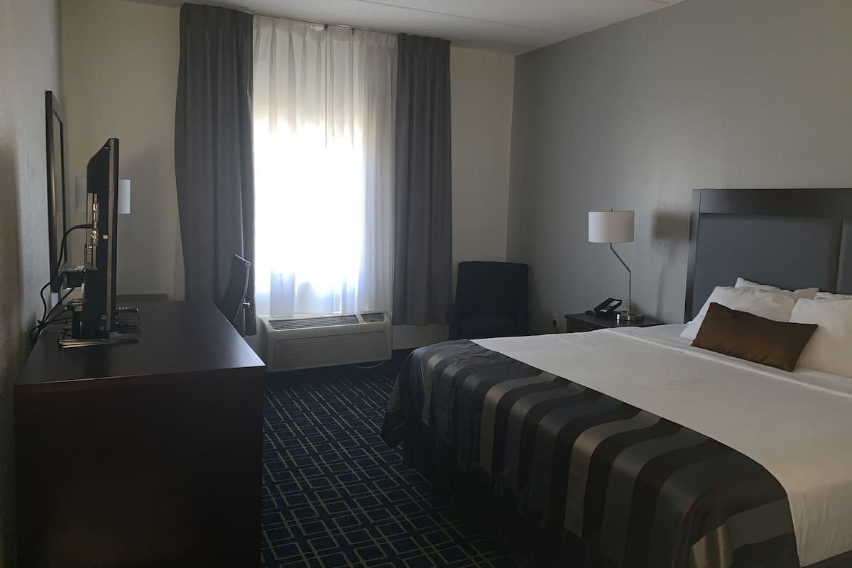 A hotel room with a bed, a desk with a computer, a chair, a lamp, and a window with curtains.