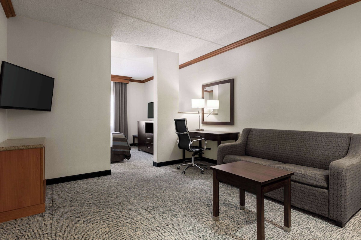 A hotel room with a flat-screen TV, a sofa, a desk with a chair, and a small table.