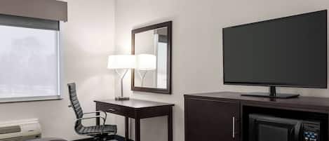 A hotel room with a bed, desk, chair, lamp, television, and microwave.