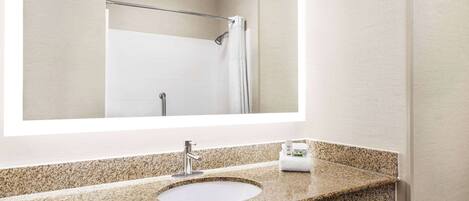 A bathroom with a granite countertop sink, a mirror, and a shower area.