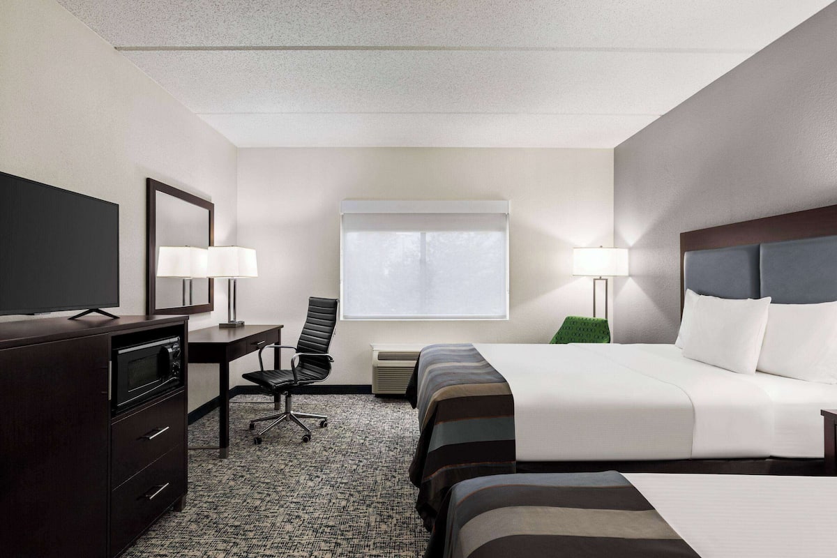 A hotel room with a bed, a desk with a chair, a television, and a window with blinds.