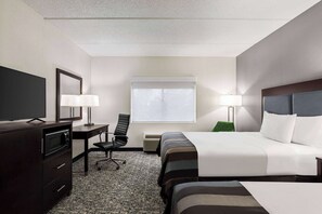 A hotel room with a bed, a desk with a chair, a television, and a window with blinds.