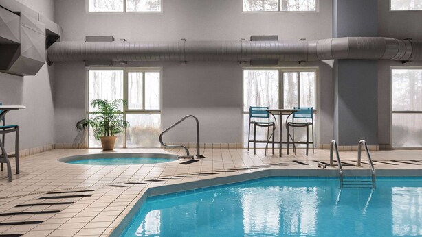 An indoor swimming pool with tiled flooring, a potted plant, and two chairs.