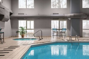 An indoor swimming pool with tiled flooring, a potted plant, and two chairs.