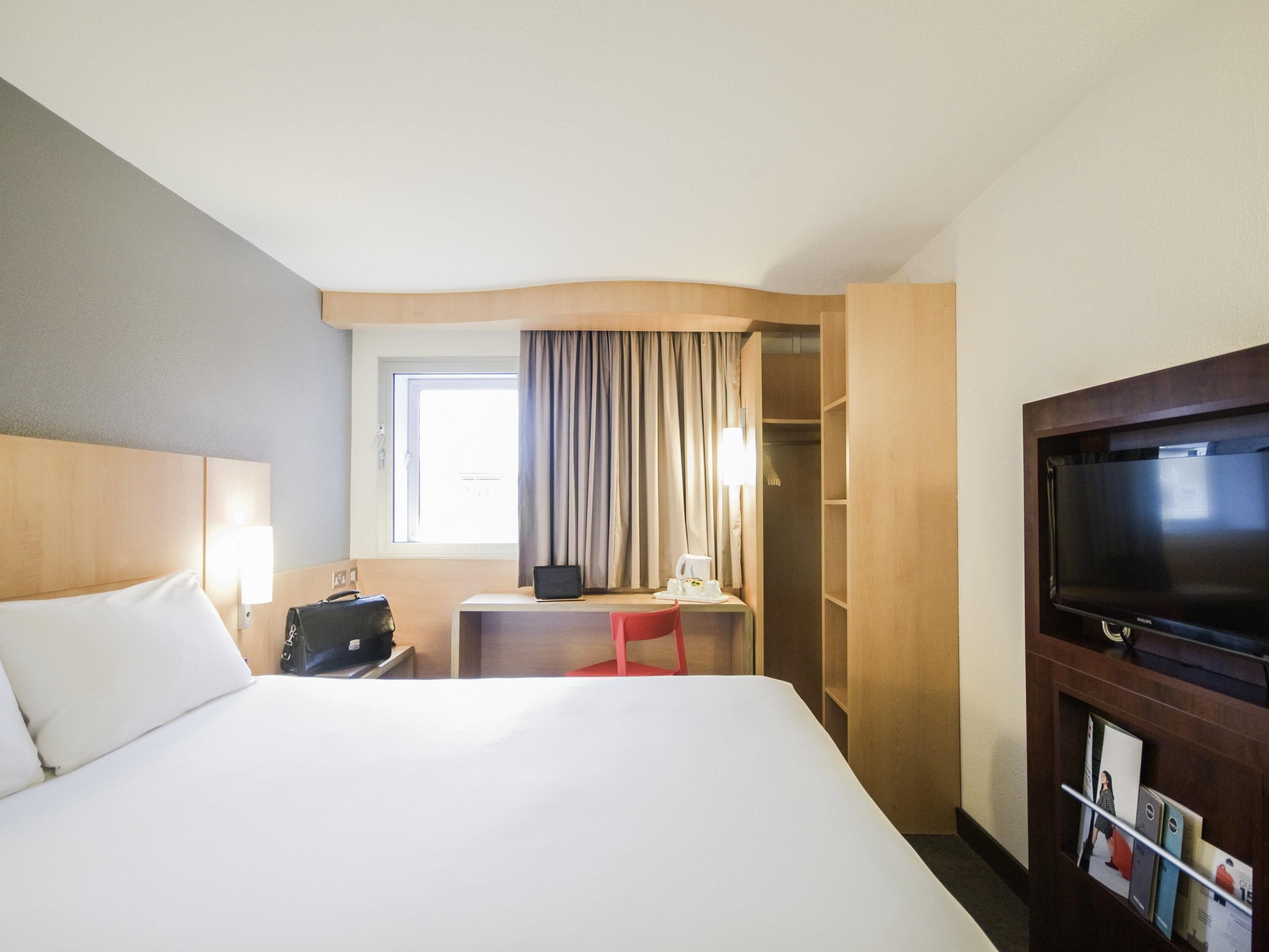Ett hotellrum med en stor säng, ett skrivbord med en bärbar dator, en tv och en garderob.