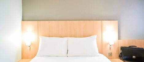 A hotel room with a wooden headboard, two bedside lamps, a bed with white linens, and a black briefcase on a nightstand.