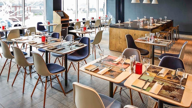 Un restaurante moderno con varias mesas y sillas, una zona de bar y grandes ventanales con vistas.