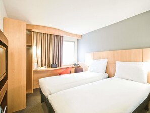 Une chambre d’hôtel avec deux lits, un bureau, une chaise, une télévision et une fenêtre avec des rideaux.