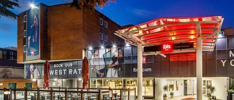 A modern hotel with a glass facade, a red awning, and a sign for 'Ibis London Heathrow'.
