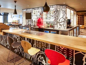 A bar area with a modern design, including a wooden counter, bar stools, and a wall with abstract art.
