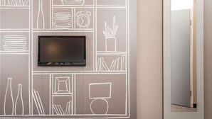 Una pared con un televisor de pantalla plana montado sobre un mural estilo pizarra que representa diversos objetos como libros, una radio y un reloj.