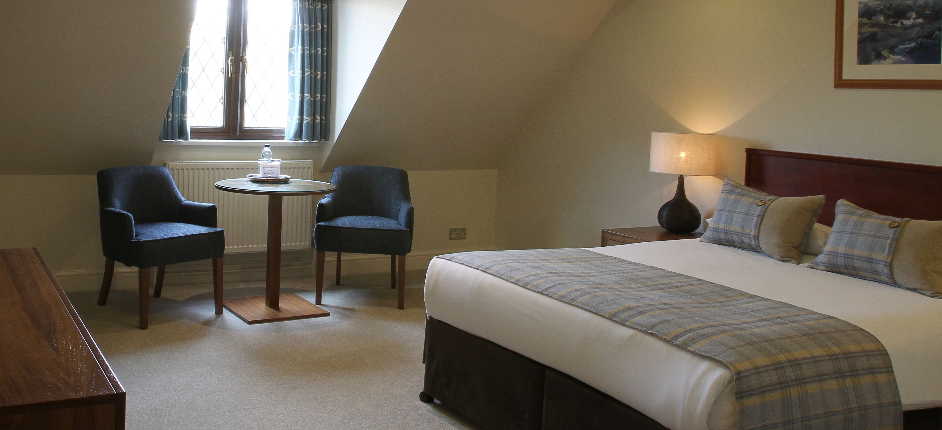 Een hotelkamer met een bed, twee stoelen, een kleine tafel en een lamp.