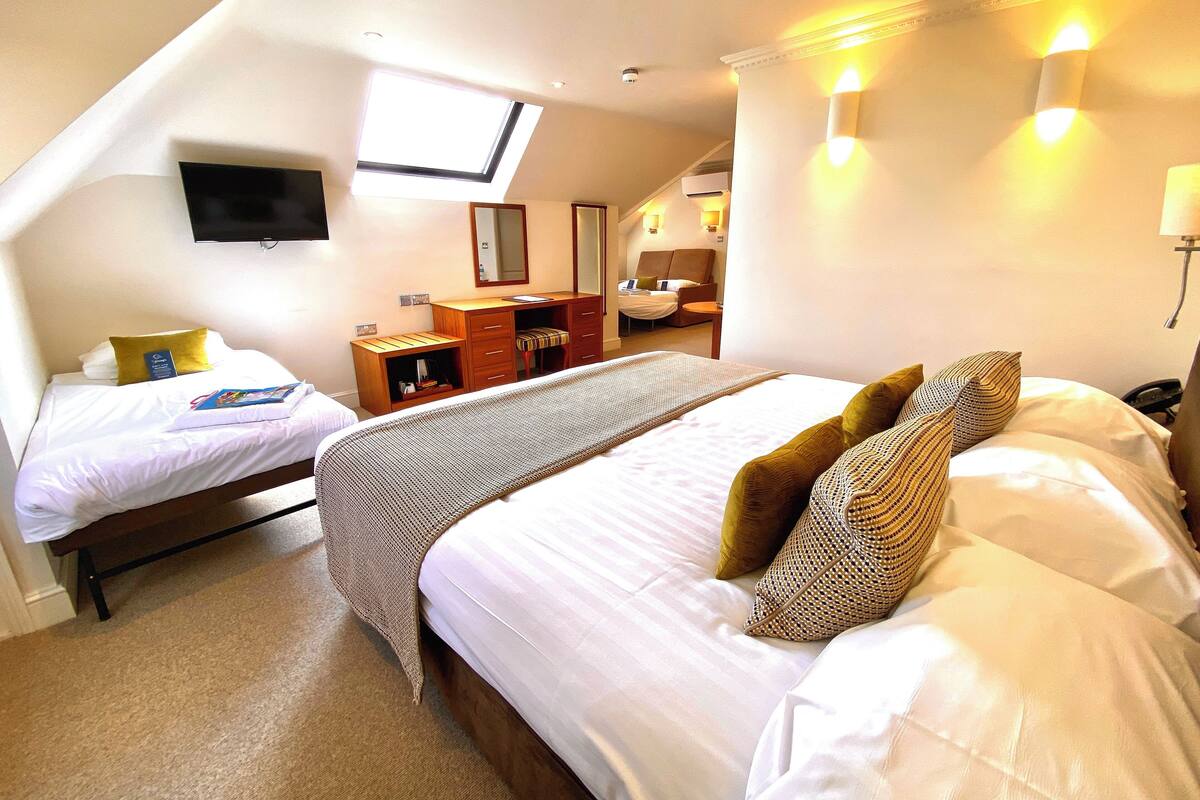A hotel room with two beds, a desk, a chair, a TV, and a skylight.