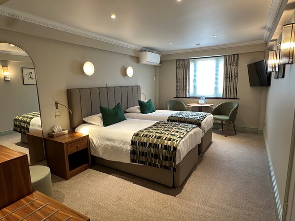 A hotel room with two beds, a desk, chairs, a TV, and a window with curtains.
