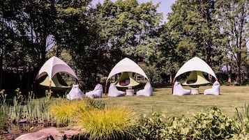 Three white tents with curved roofs in a grassy area with a pond and trees in the background.