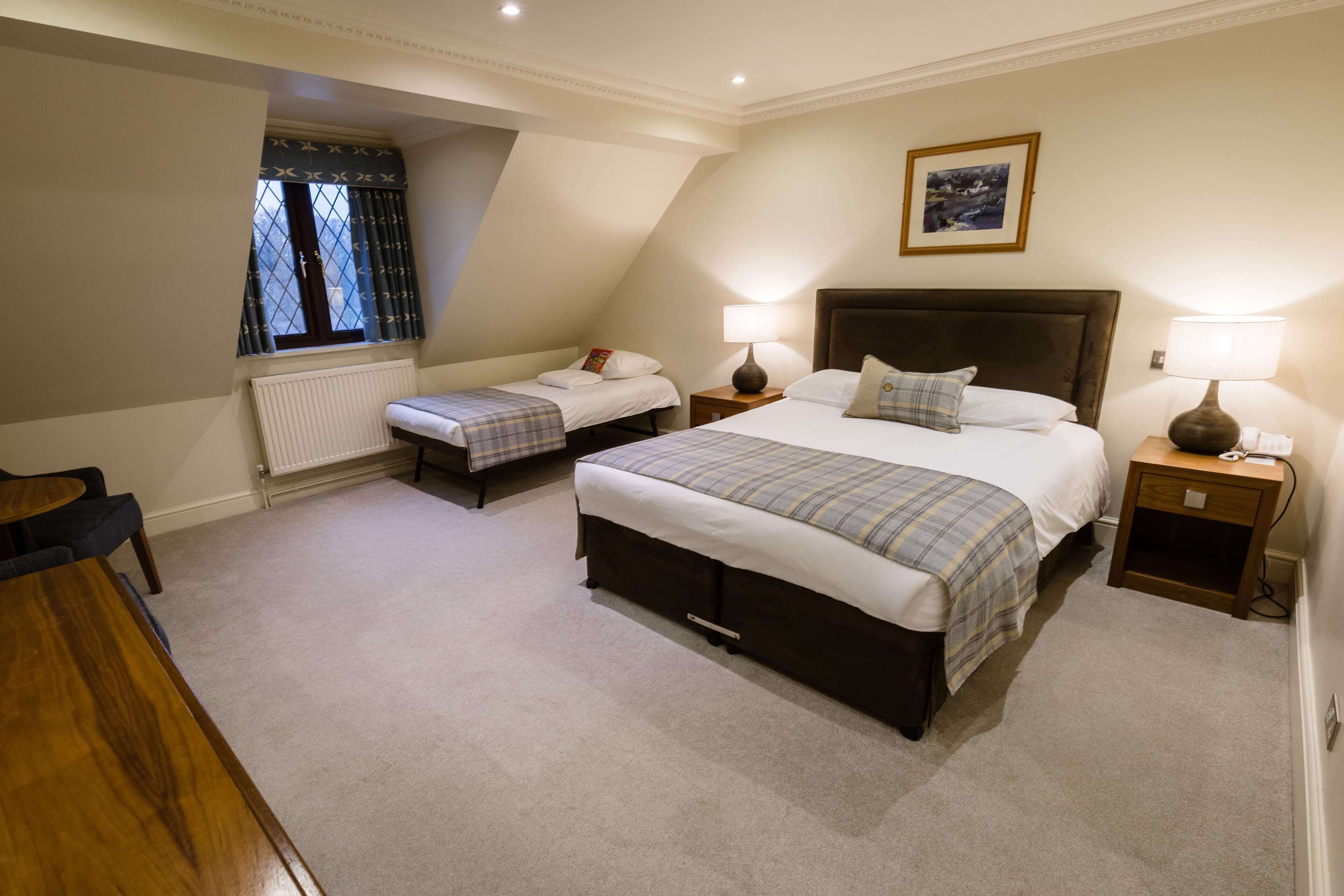A bedroom with two beds, a wooden table, and a window with curtains.