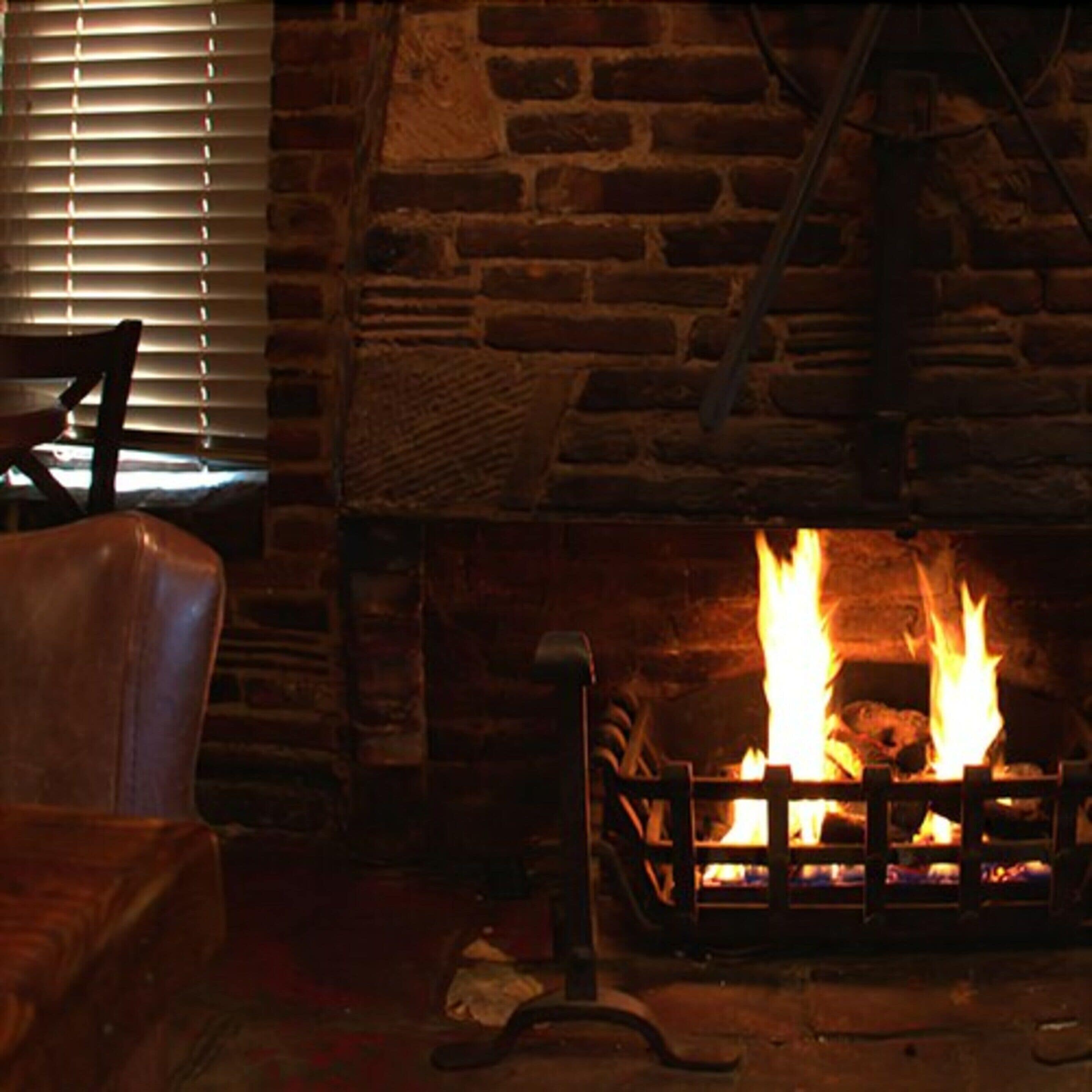 A room with a stone fireplace, a leather chair, and a window with blinds.