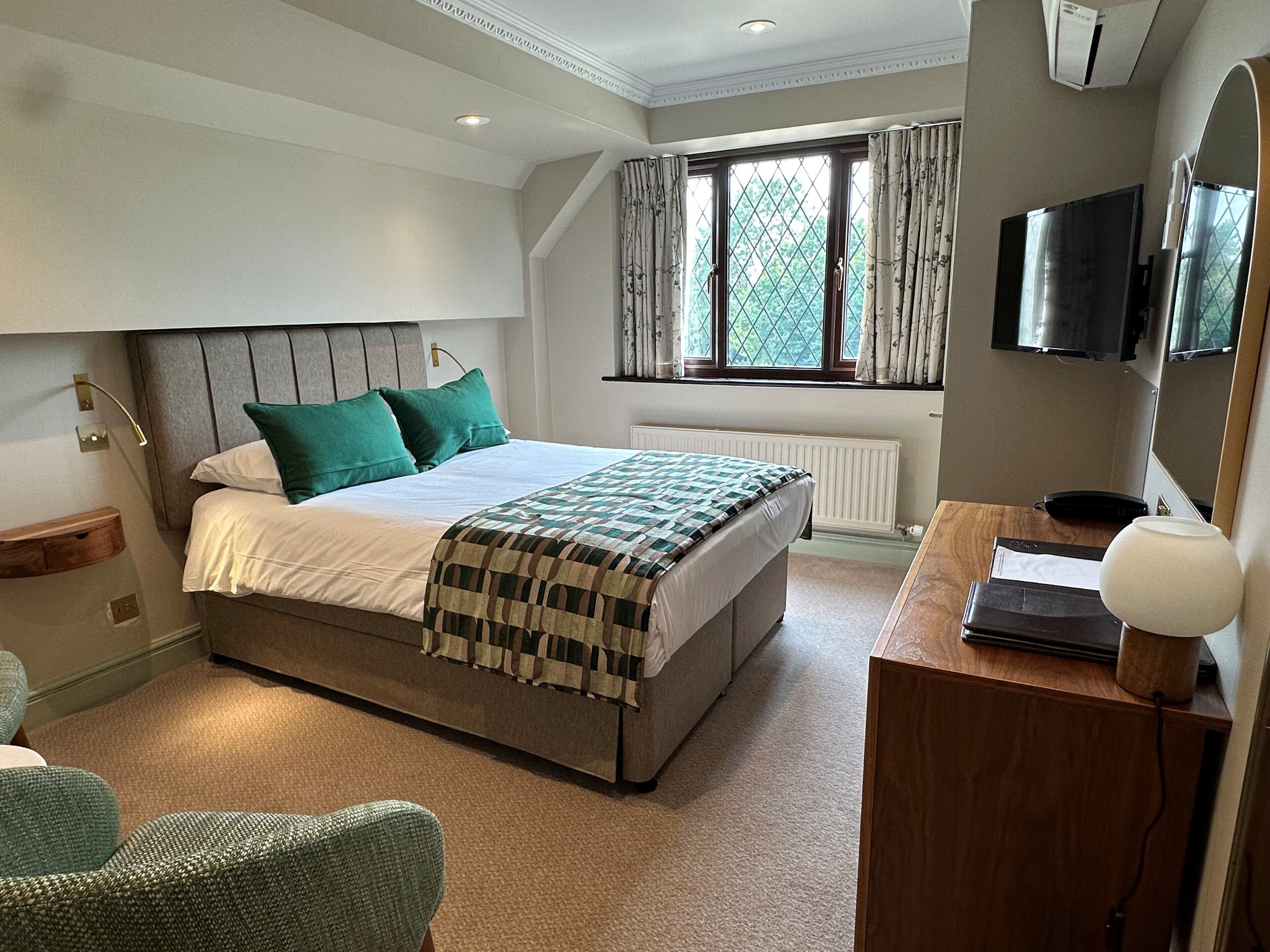 A bedroom with a bed, a desk, a chair, a television, and a window with curtains.