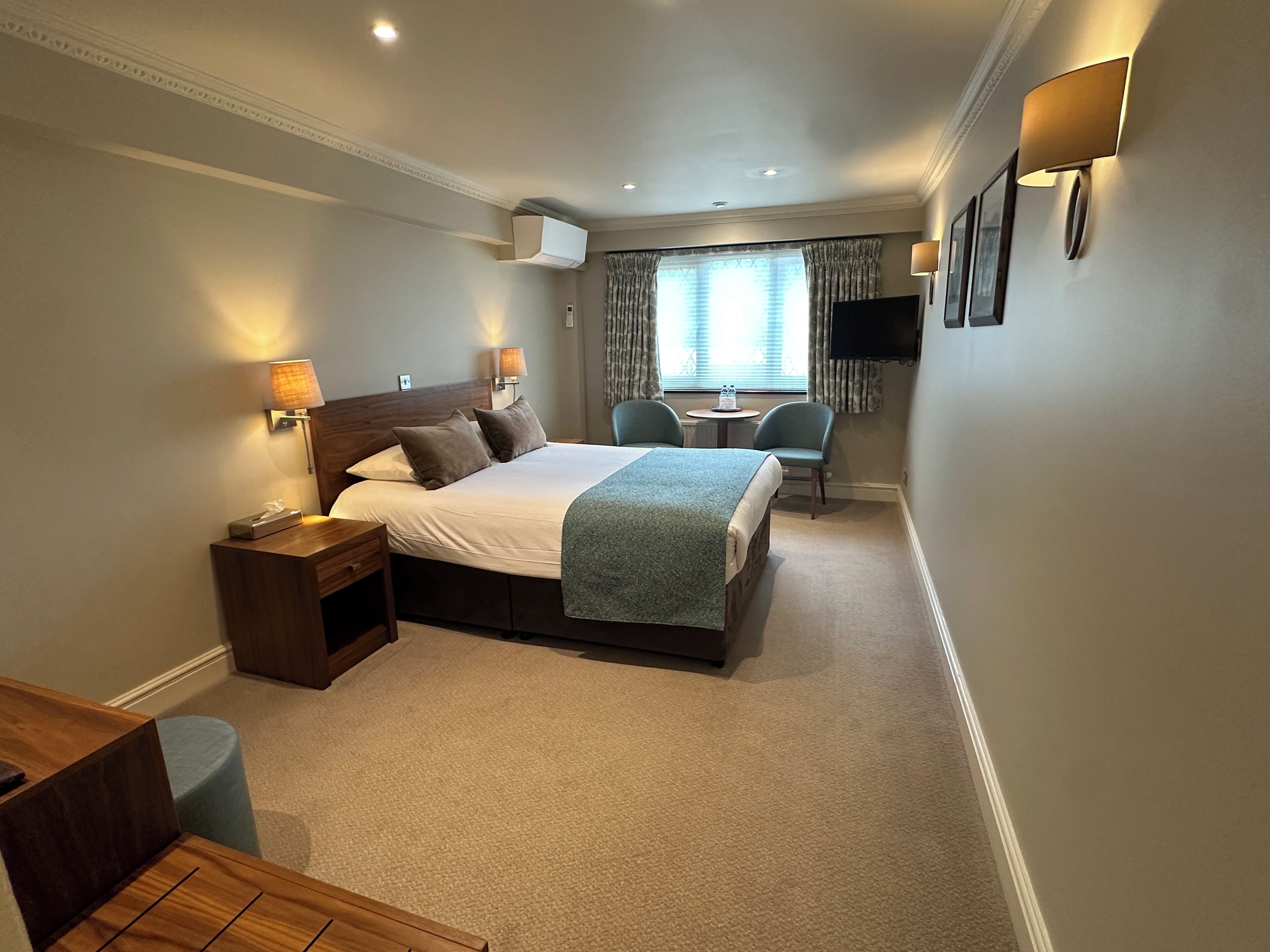 A hotel room with a large bed, bedside tables, a desk, a chair, a TV, and a window with curtains.