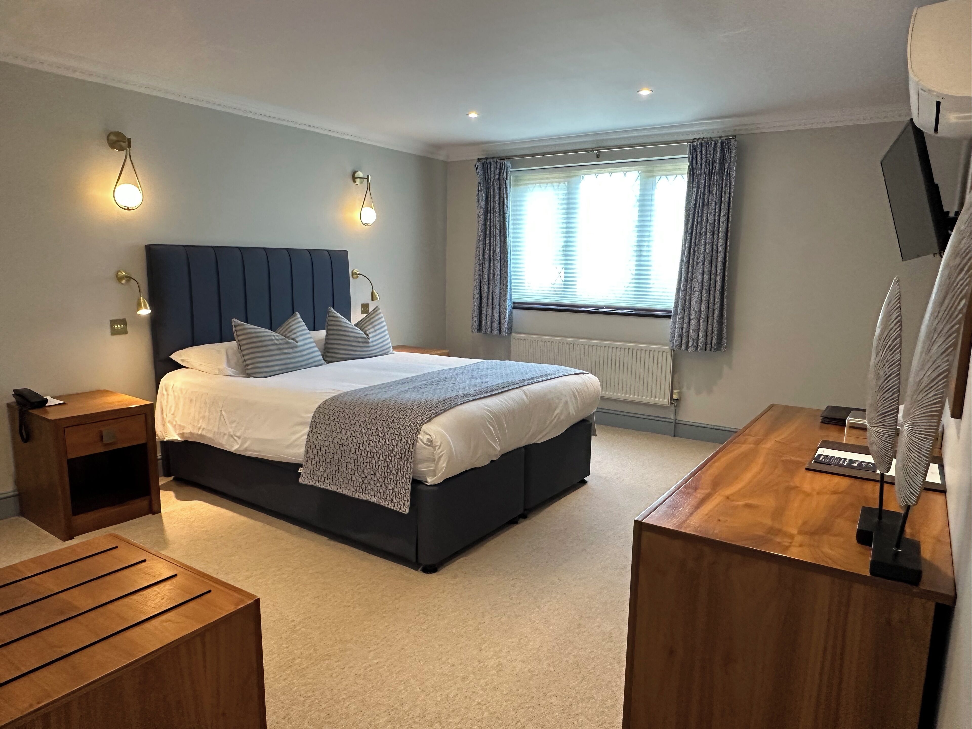 A modern bedroom with a large bed, bedside tables, a desk, and a window with curtains.