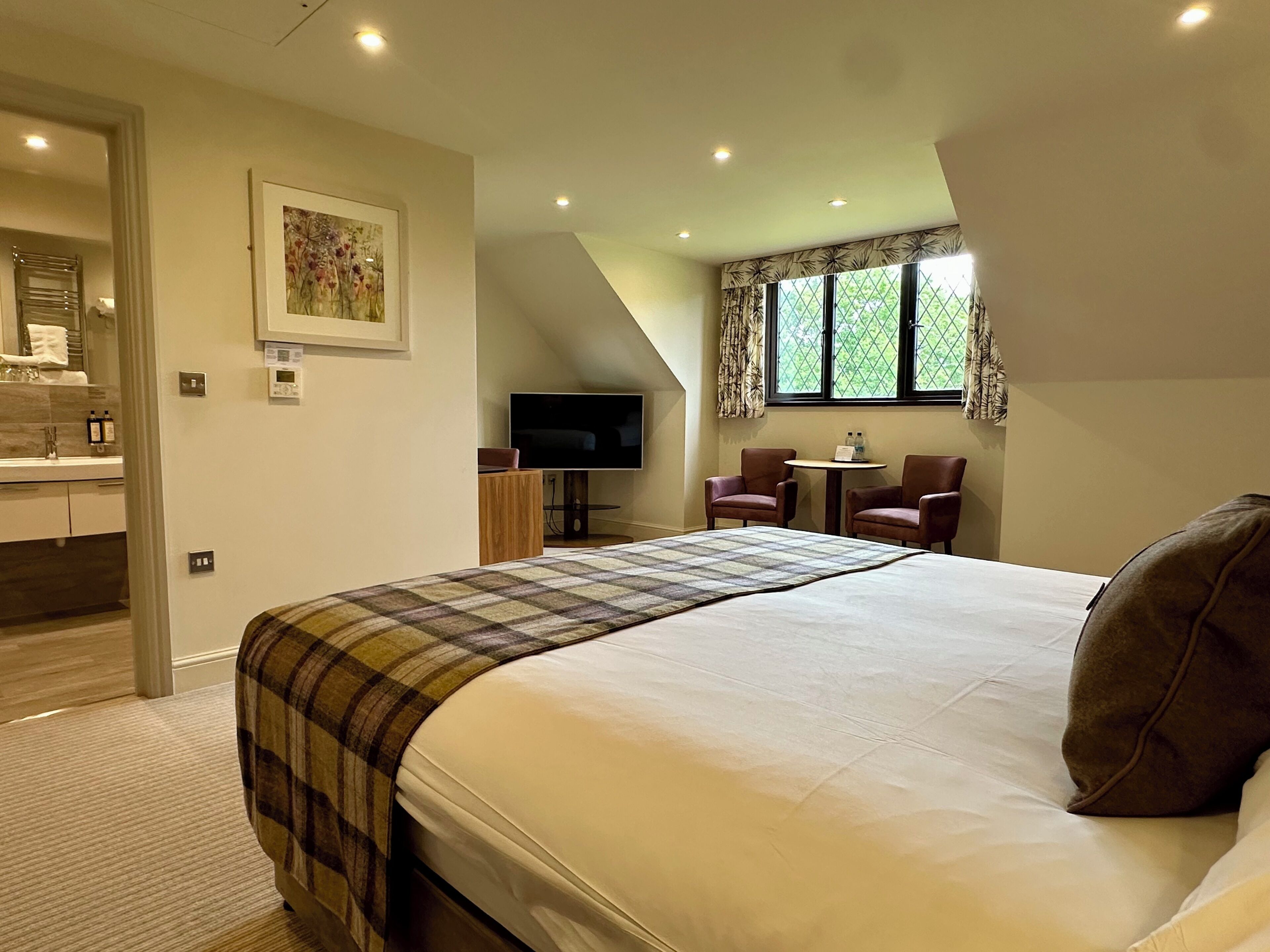 A bedroom with a large bed, a TV, a small table, and two chairs.