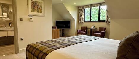 A bedroom with a large bed, a TV, a small table, and two chairs.