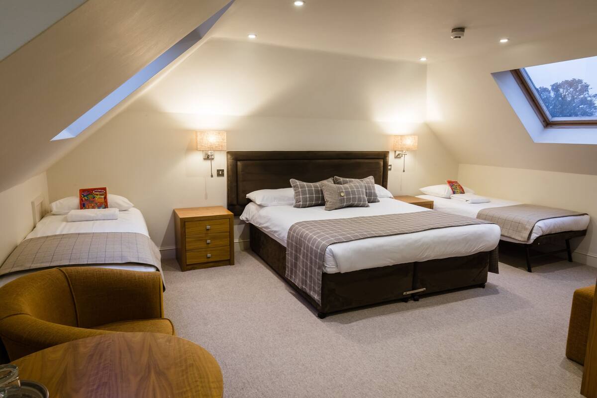 A bedroom with a large bed, two smaller beds, a desk, and a chair. There is a skylight above the large bed.