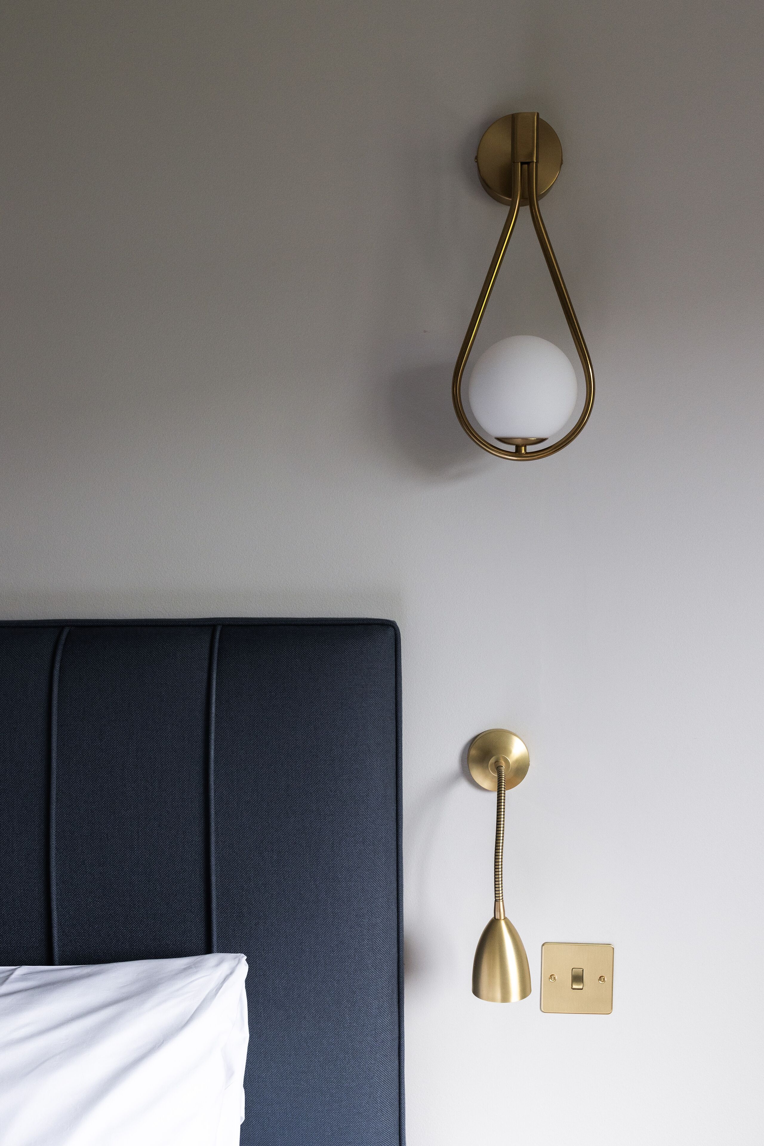 A bed with a dark headboard, a wall-mounted light fixture with a spherical shade, and a switch.