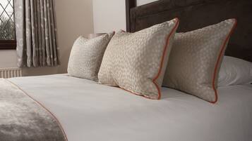A neatly made bed with a patterned pillow and a plain pillow, a window with curtains, and a wooden headboard.