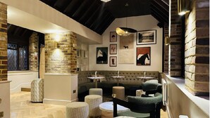 A cozy lounge area with a stone wall, cushioned seating, and artwork on the walls. - Stirrups Hotel (Bracknell)