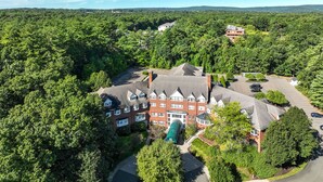 A large, multi-story building surrounded by dense forest, with a parking lot and a small green structure nearby. - Simsbury Inn (Weatogue)