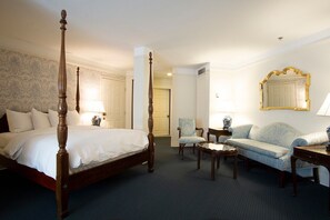 A four-poster bed with a wooden frame, a light blue sofa, a small round table, and a chair.