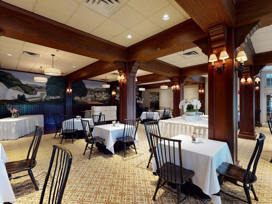 Un comedor espacioso con techos altos, vigas de madera y varias mesas con manteles blancos.