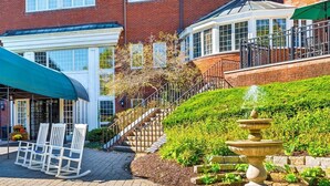 A brick building with a covered patio, a fountain, and a staircase leading to a second floor. - Simsbury Inn (Weatogue)