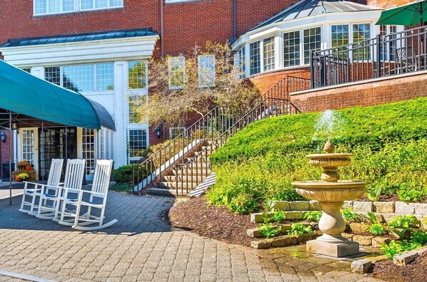 A brick building with a covered patio, a fountain, and a staircase leading to a second floor.