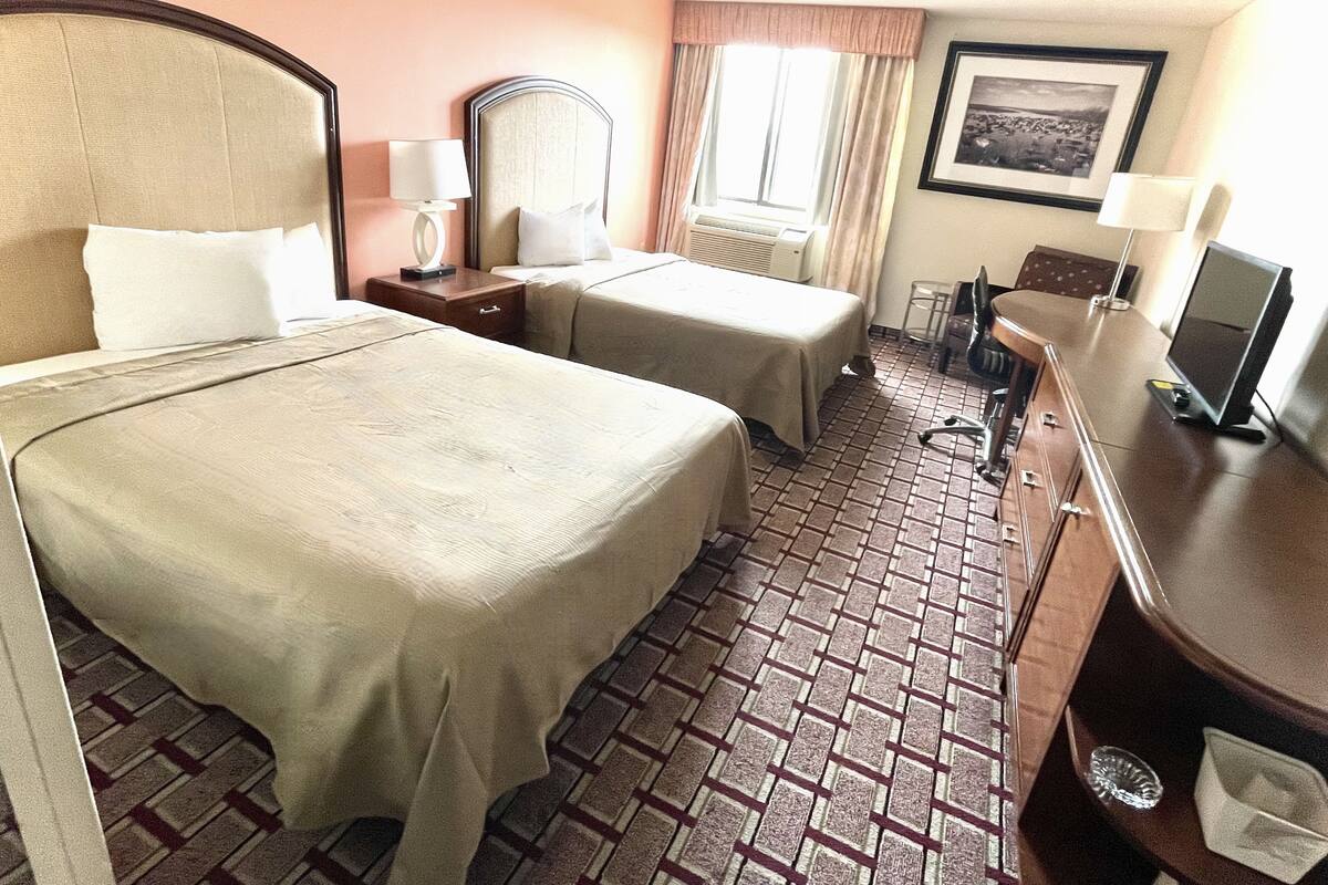 A hotel room with two beds, a desk, a chair, a television, and a window with curtains.