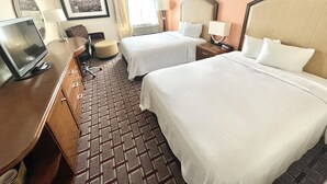 Habitación de hotel con dos camas, un escritorio con computadora, una silla y una mesita.