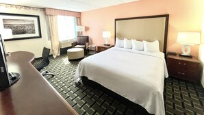 Una habitación de hotel con una cama grande, un escritorio, una silla, una mesita y una lámpara.
