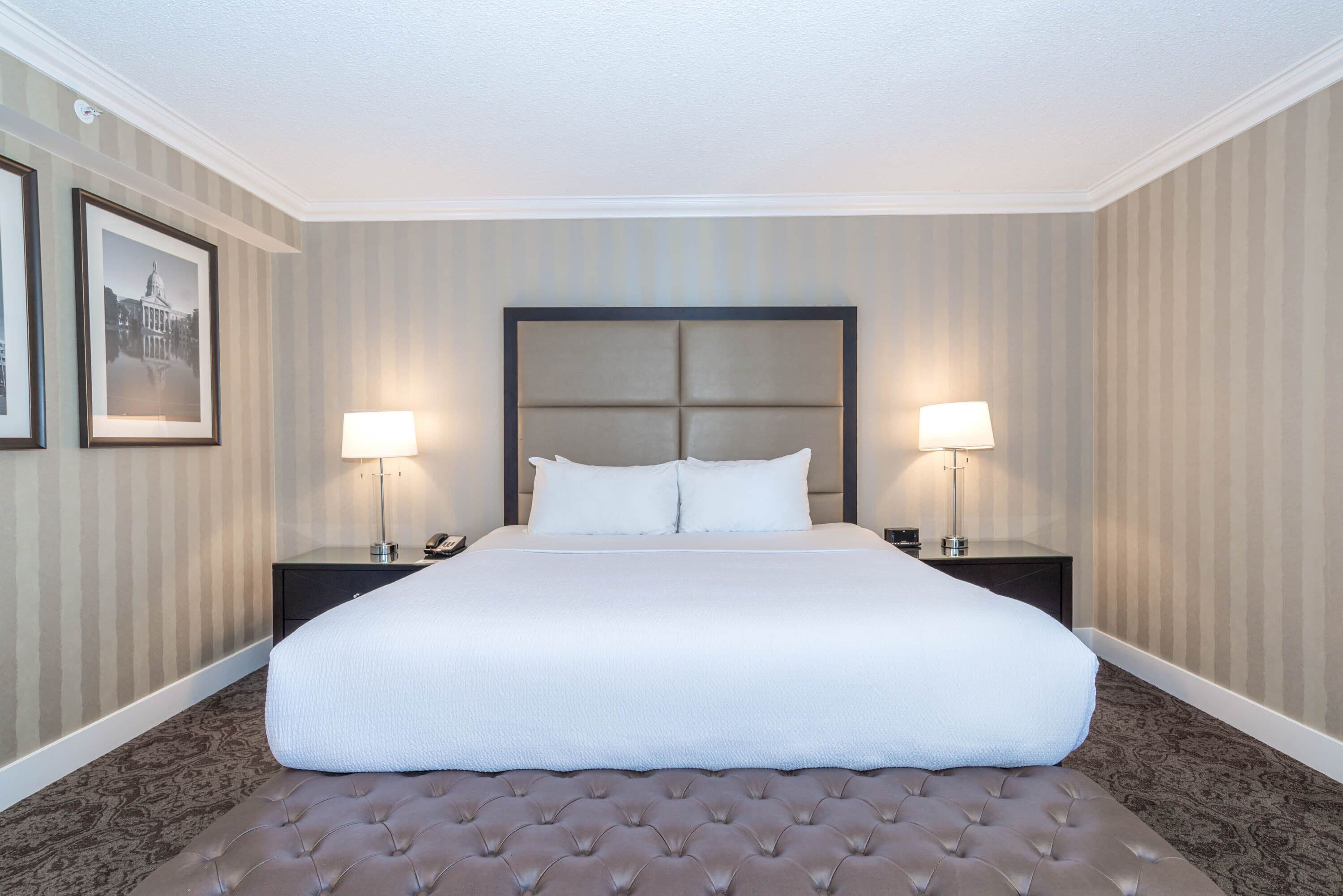 Habitación de hotel con una cama grande, dos mesitas de noche, un cabecero y un cuadro en la pared.