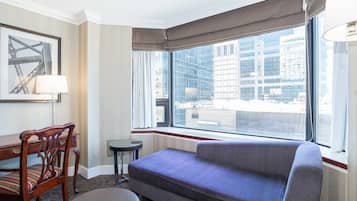 Habitación de hotel con un ventanal grande, un sofá, una silla, una mesita y una lámpara.