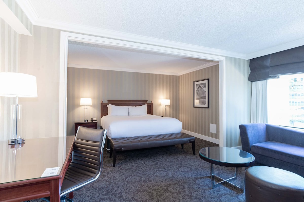 A hotel room with a bed, a desk with a chair, a small round table, and a sofa.