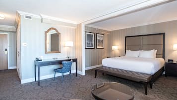 A hotel room with a large bed, a desk with a chair, a small table, and two wall-mounted lamps.