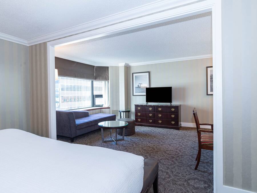 Una habitación de hotel con una cama grande, un sofá, una mesita redonda, un televisor en una cómoda y una ventana con cortinas.