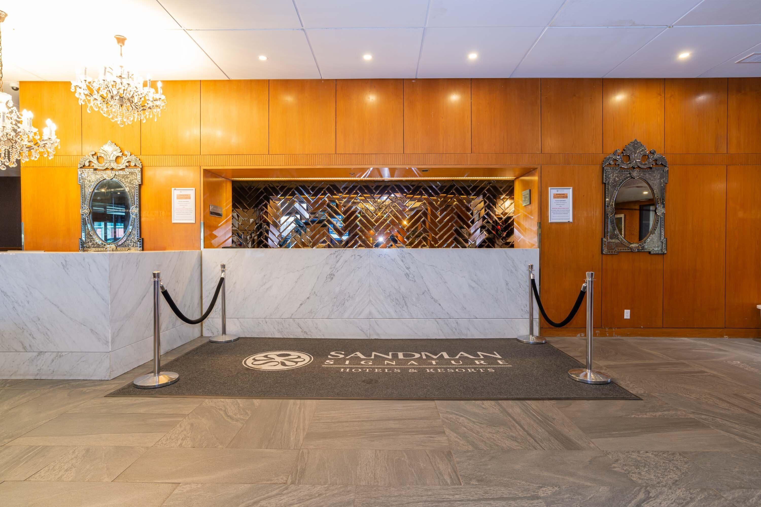 A reception area with a marble counter, wooden paneling, and a chandelier.