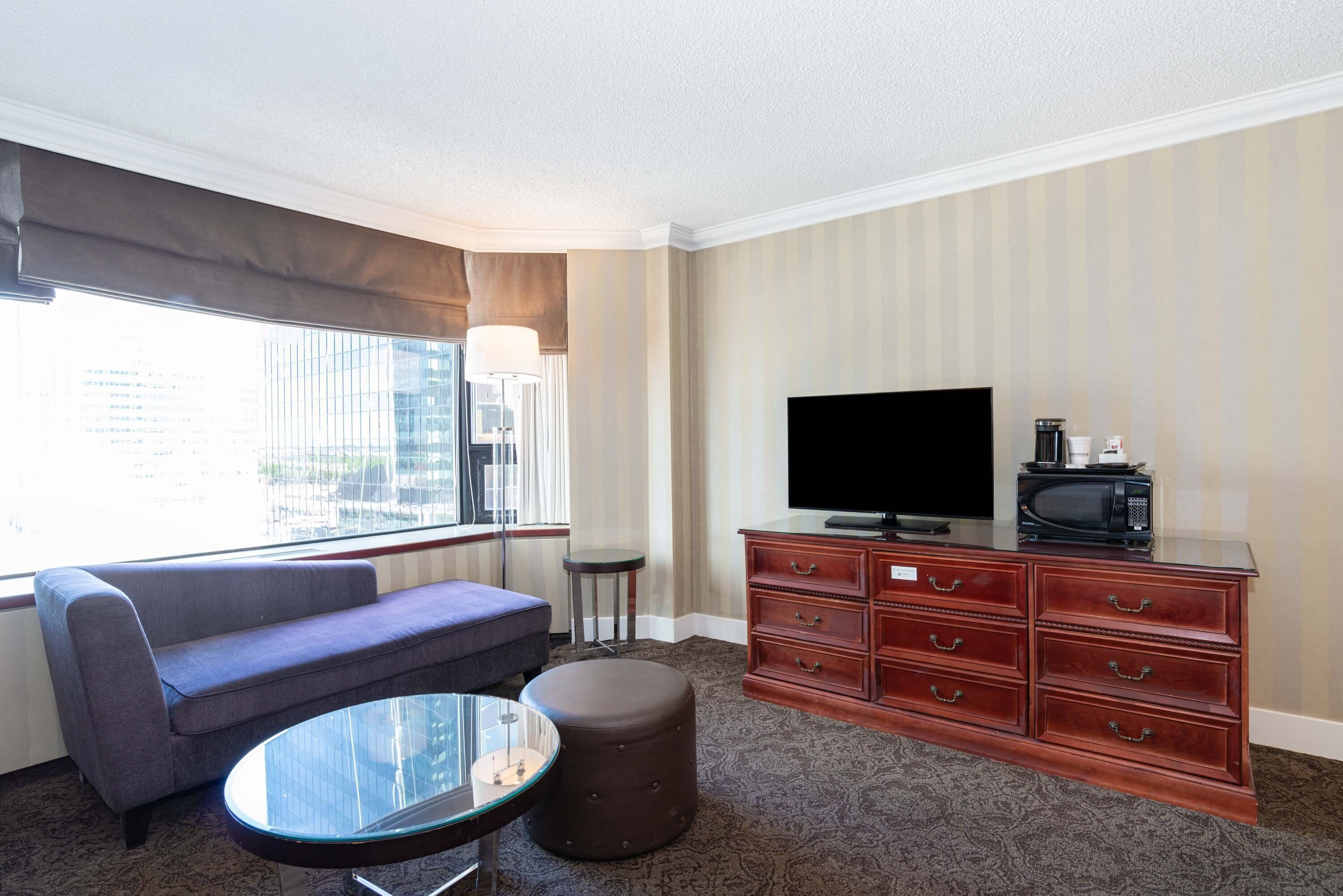 A hotel room with a sofa, ottoman, TV, and a dresser.