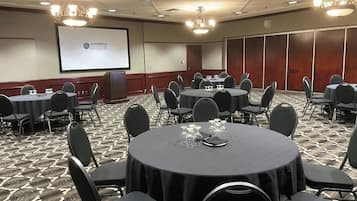 Un salón de conferencias con mesas redondas, sillas negras y una pantalla proyectora mostrando 'SANDMAN SIGNATURE'.