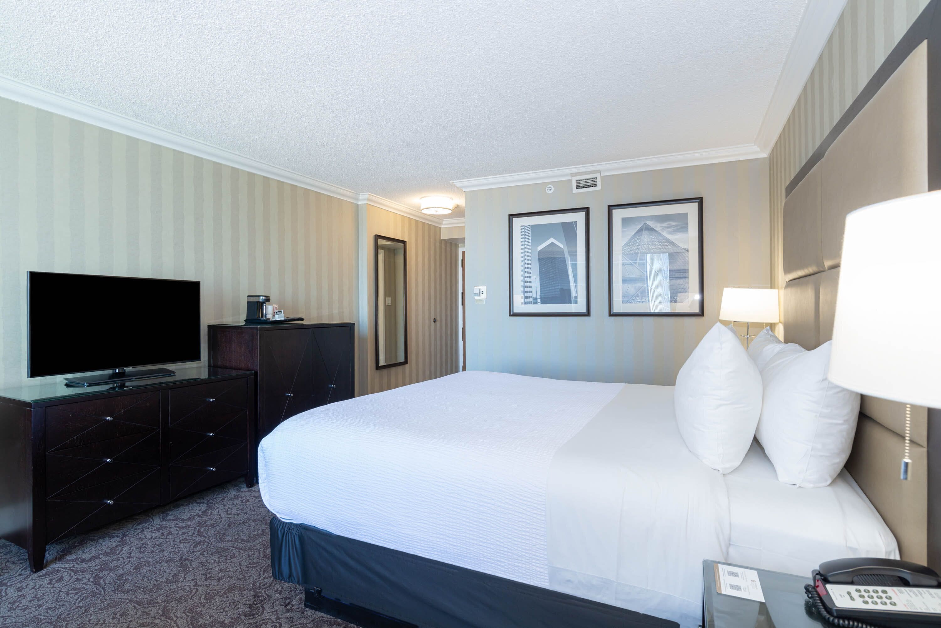 Une chambre d’hôtel avec un grand lit, un téléviseur à écran plat, une commode et une table de chevet avec une lampe et un téléphone.