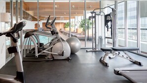 A modern gym with exercise equipment, a bench, and a view of a pool and outdoor seating. - Sandman Signature Edmonton Downtown Hotel (Edmonton)
