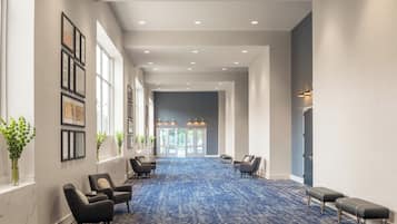 Un pasillo de hotel con alfombra azul, certificados enmarcados en las paredes y áreas de descanso con sillas y bancos.